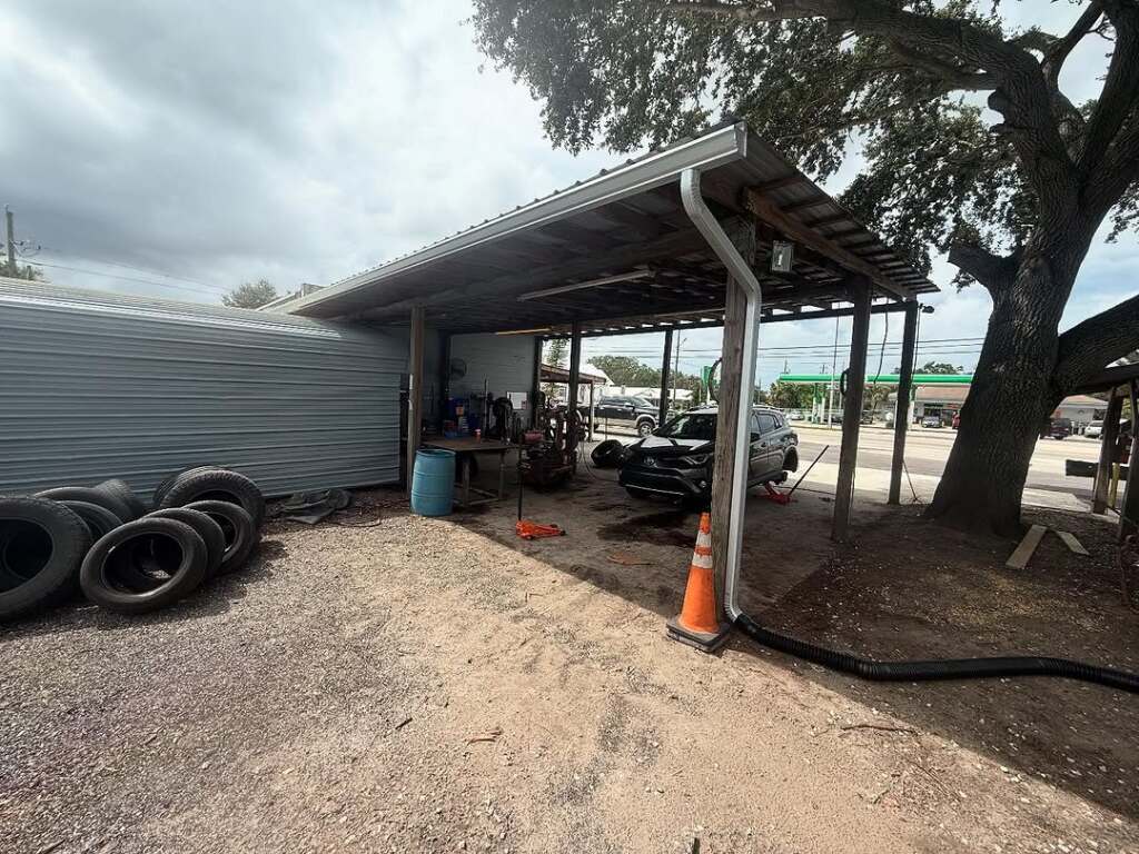 Outdoor auto repair shop with car under a carport and spare tires nearby