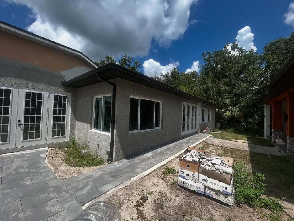 Backyard view of modern house with patio doors and paver walkway under blue sky.