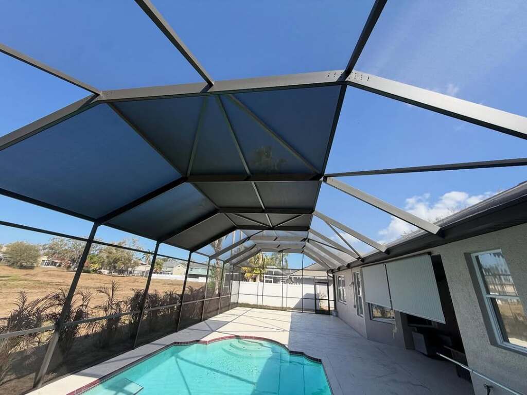Spacious screened patio with clear pool under a blue sky by residential home.