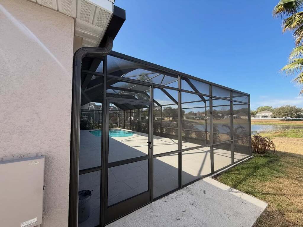 Outdoor screened patio enclosure beside a tranquil lake under clear blue sky.