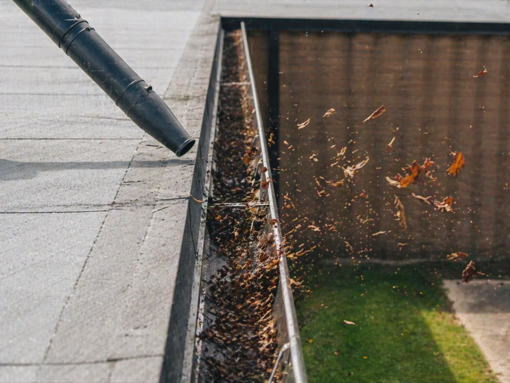 Leaf blower cleaning rooftop gutters, removing leaves and debris