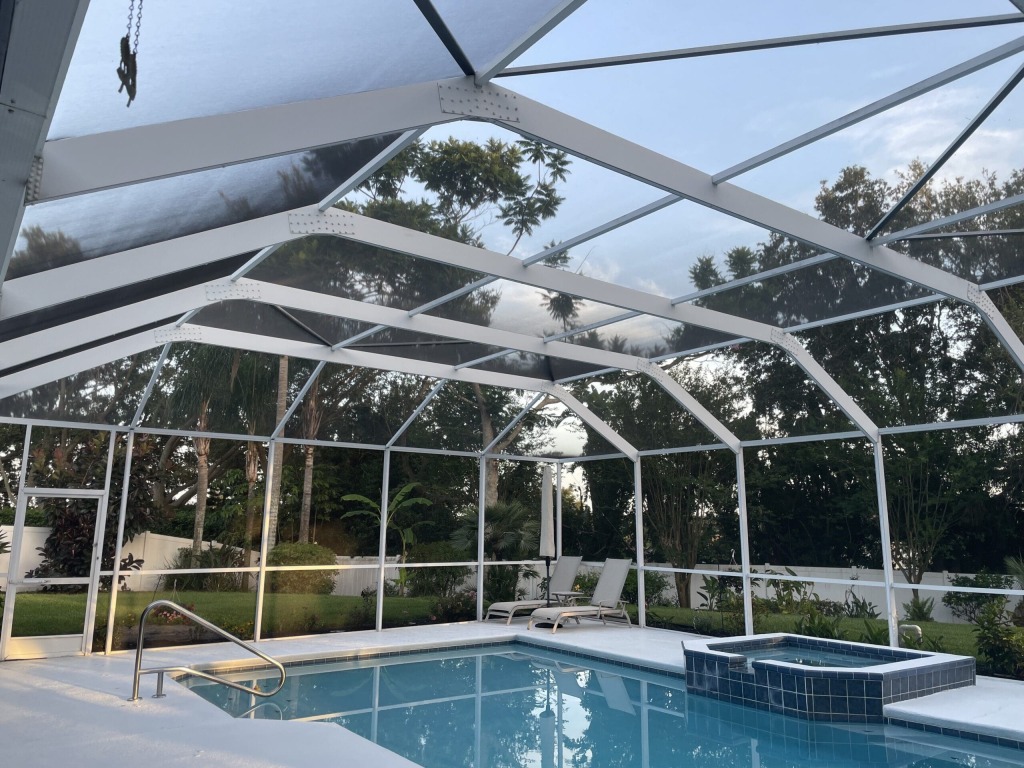 Outdoor pool and spa under a screened enclosure with lush greenery outside.