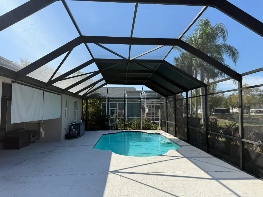 Enclosed backyard pool with screen walls and ceiling in a spacious patio setting.