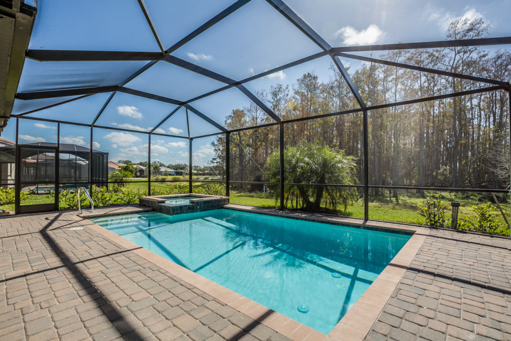 Screen-enclosed pool with hot tub and scenic nature view