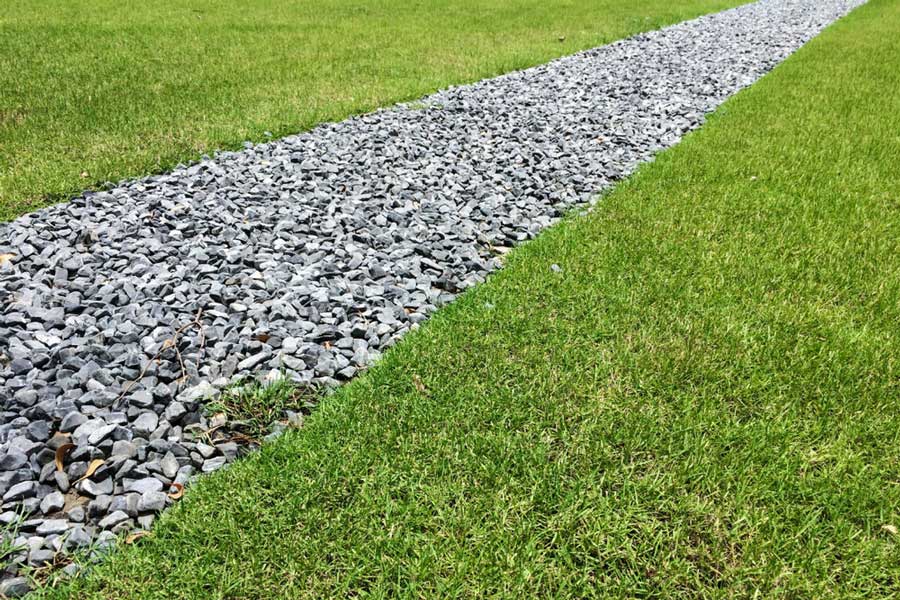 Gravel path cutting through a lush green lawn under clear sunshine.