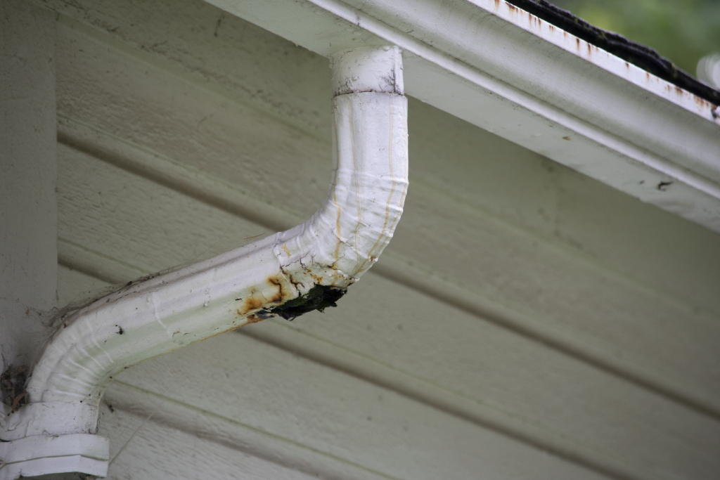 Close-up of a rusted and damaged white gutter on a house corner