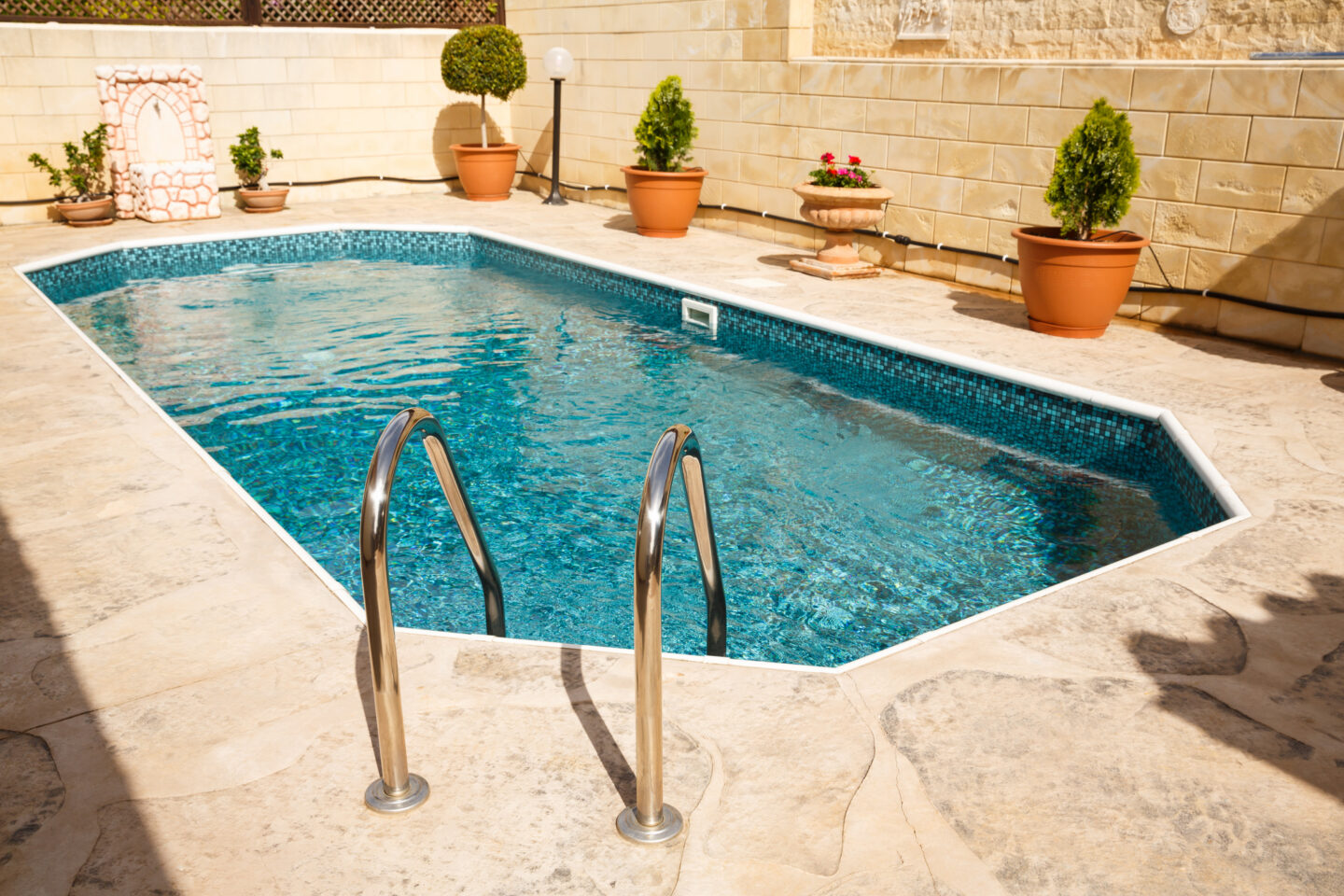 Backyard swimming pool with ladder and stone patio.