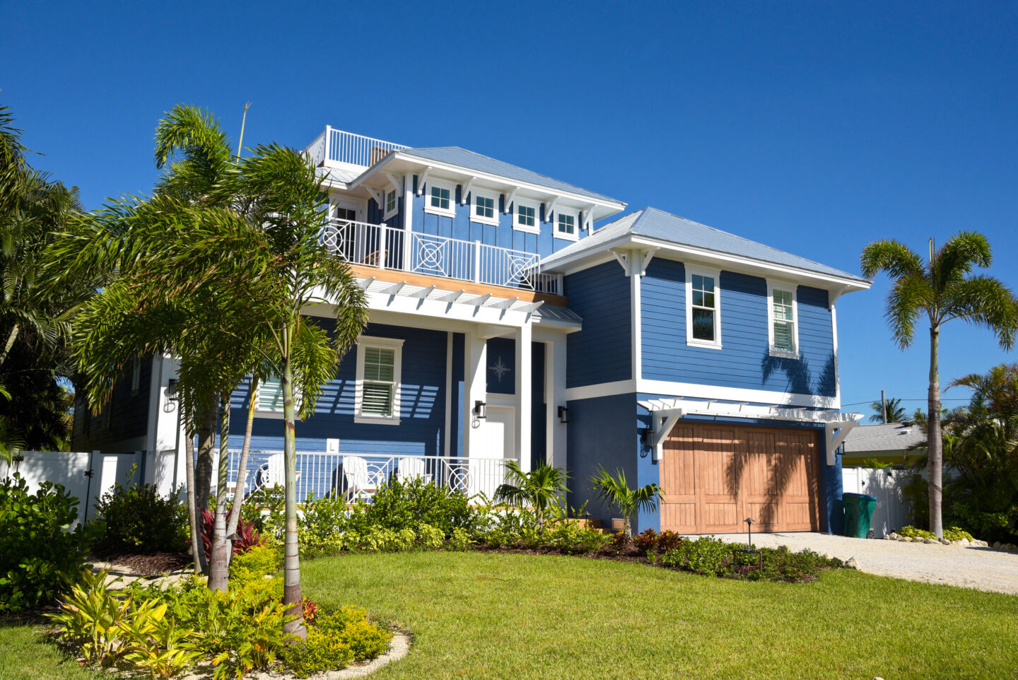 Beautiful two-story blue house with palm trees under a clear blue sky.
