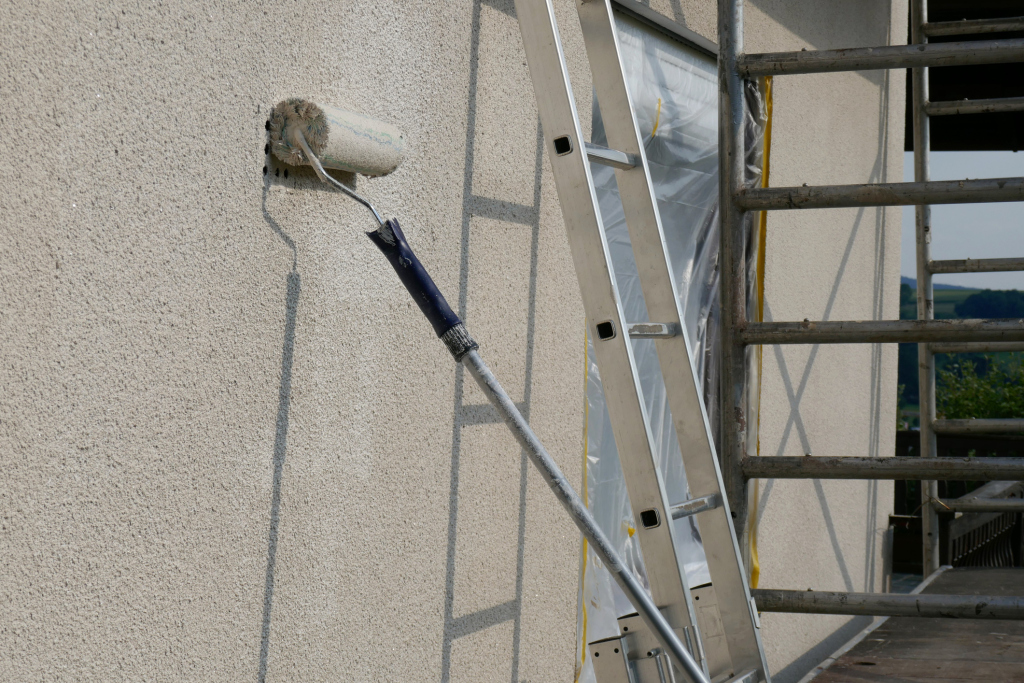Roller painting exterior wall with ladder and scaffolding