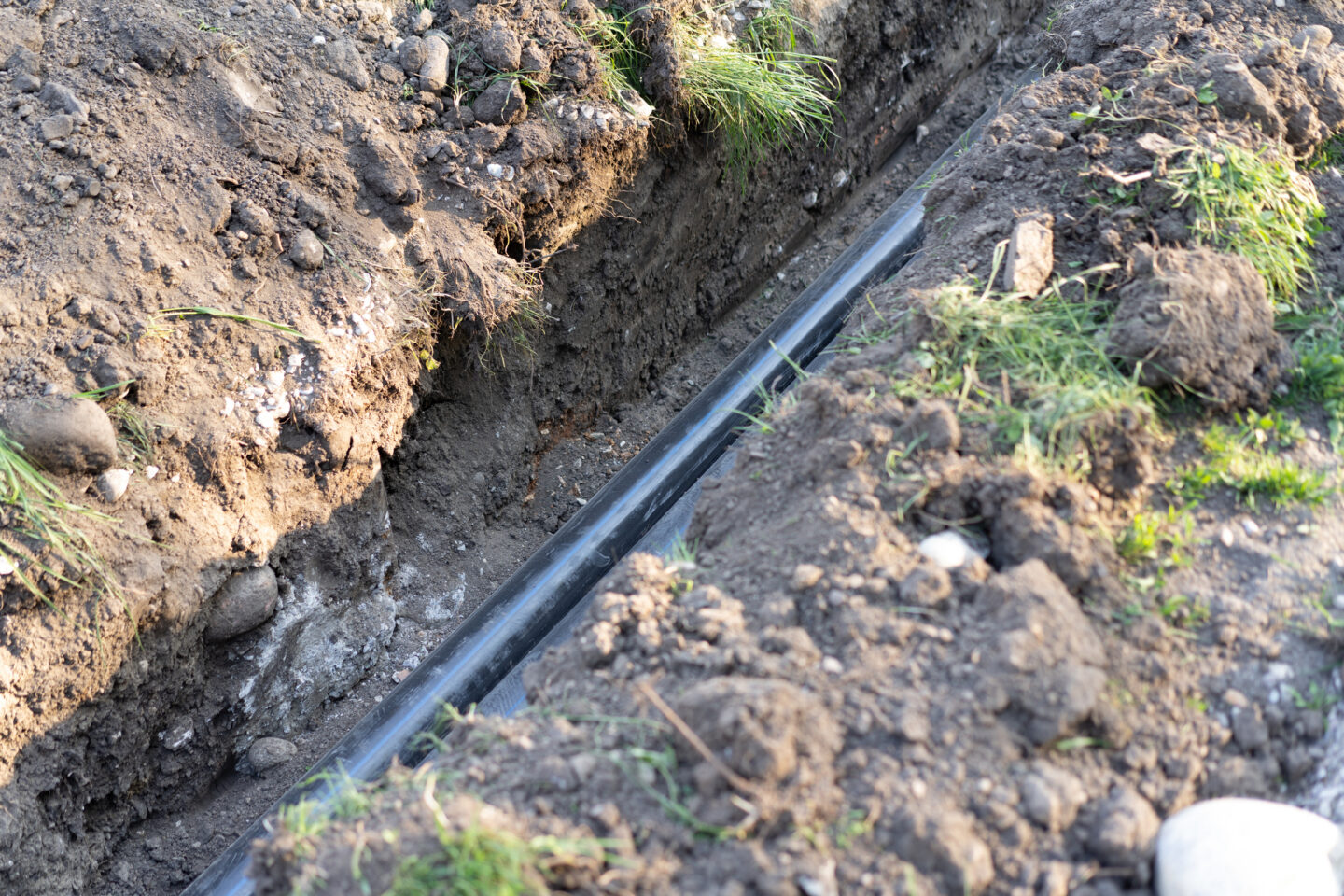 Recently dug trench with black pipe visible in the soil.
