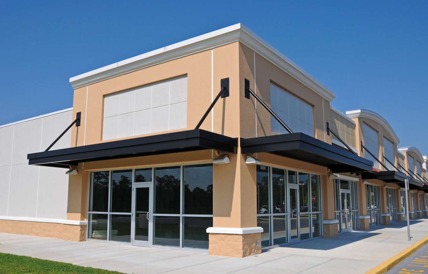 Empty storefront units in a modern shopping plaza under a clear blue sky.