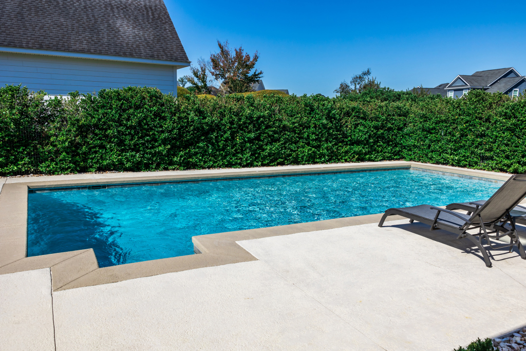 Outdoor residential swimming pool with sun loungers and vibrant greenery.