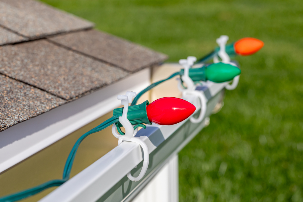 Colorful Christmas lights attached to a house gutter in daylight.