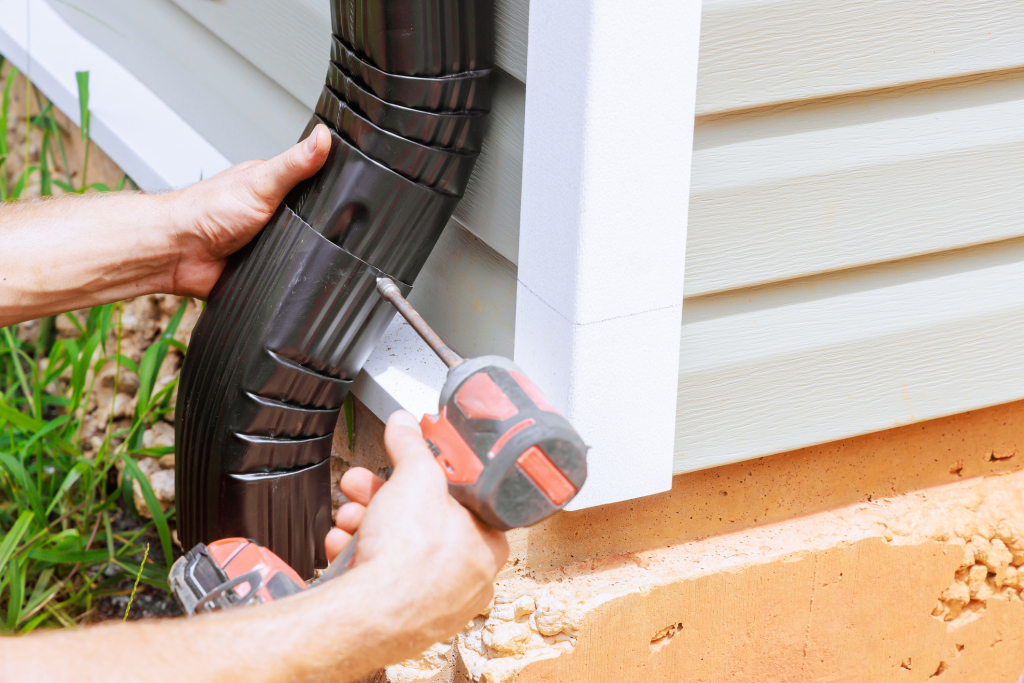 Person using a power drill to install a black gutter pipe