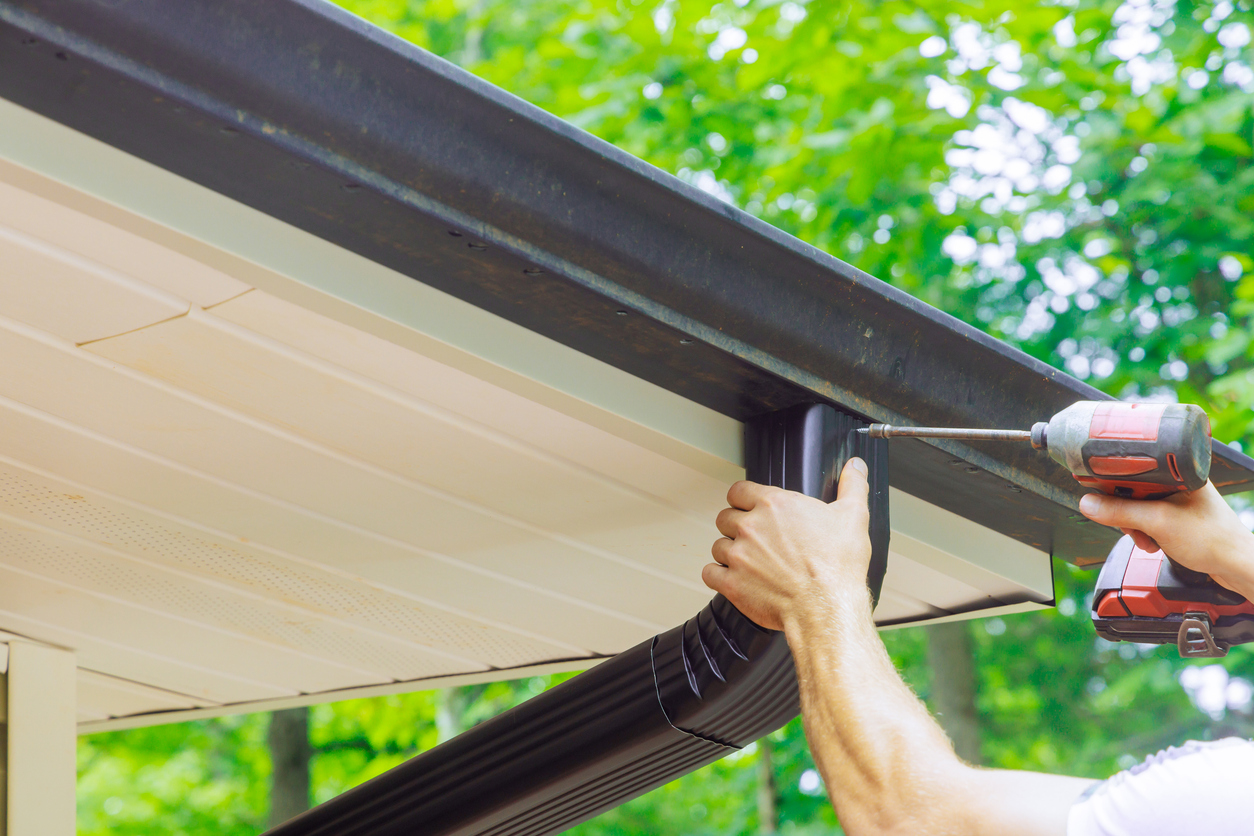 A person using a power drill to install rain gutter drainage.