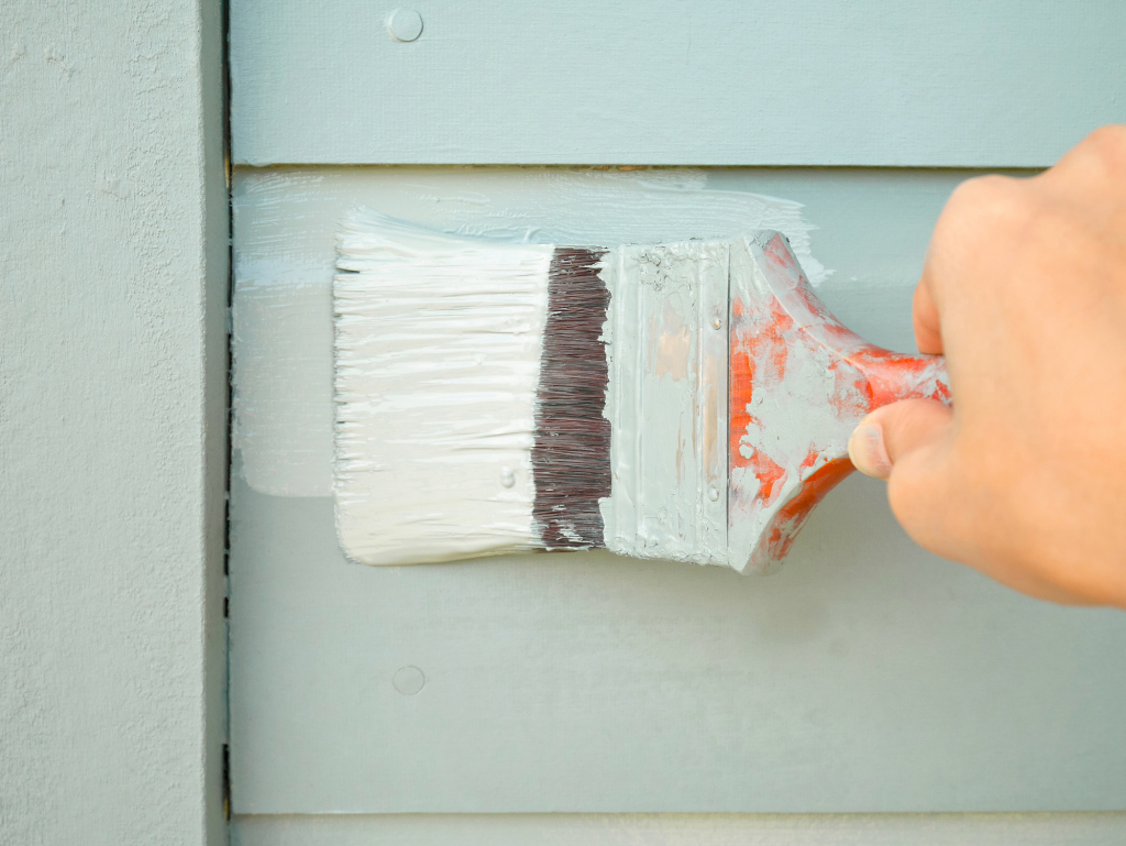 Close-up of hand painting a house exterior with a wide brush