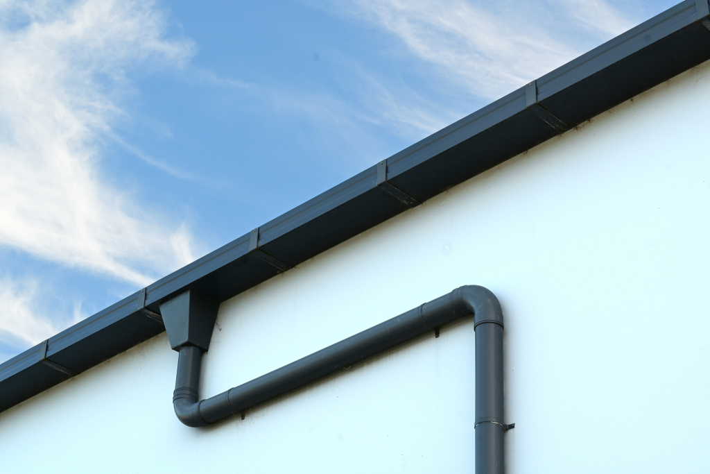 Close-up of a black gutter on a modern building against a blue sky.