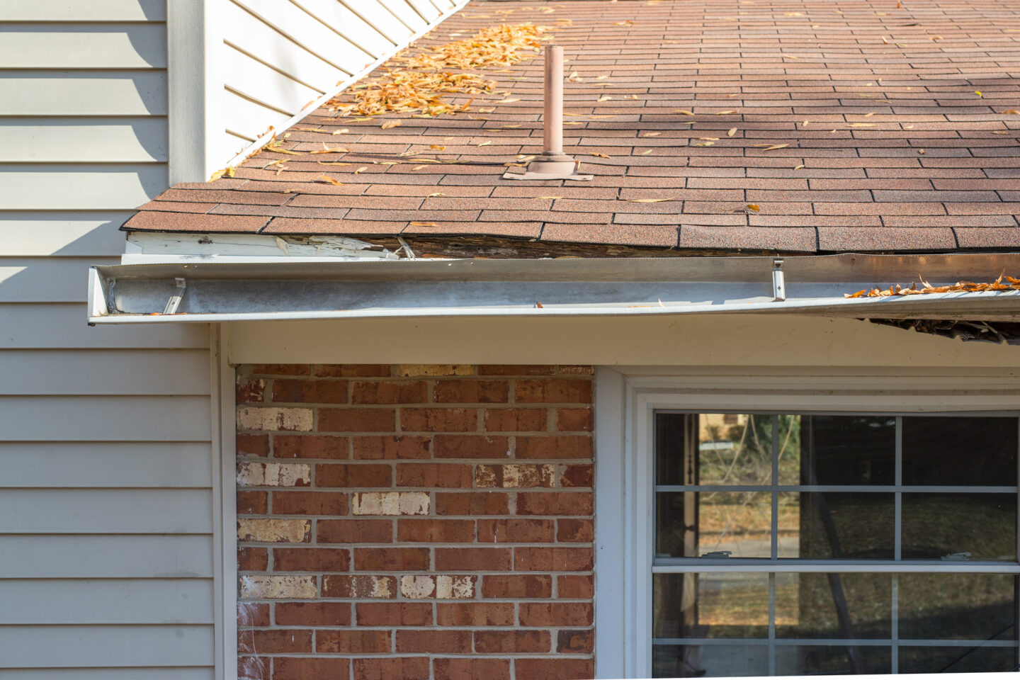 Damaged roof with debris in gutter and deteriorating shingles