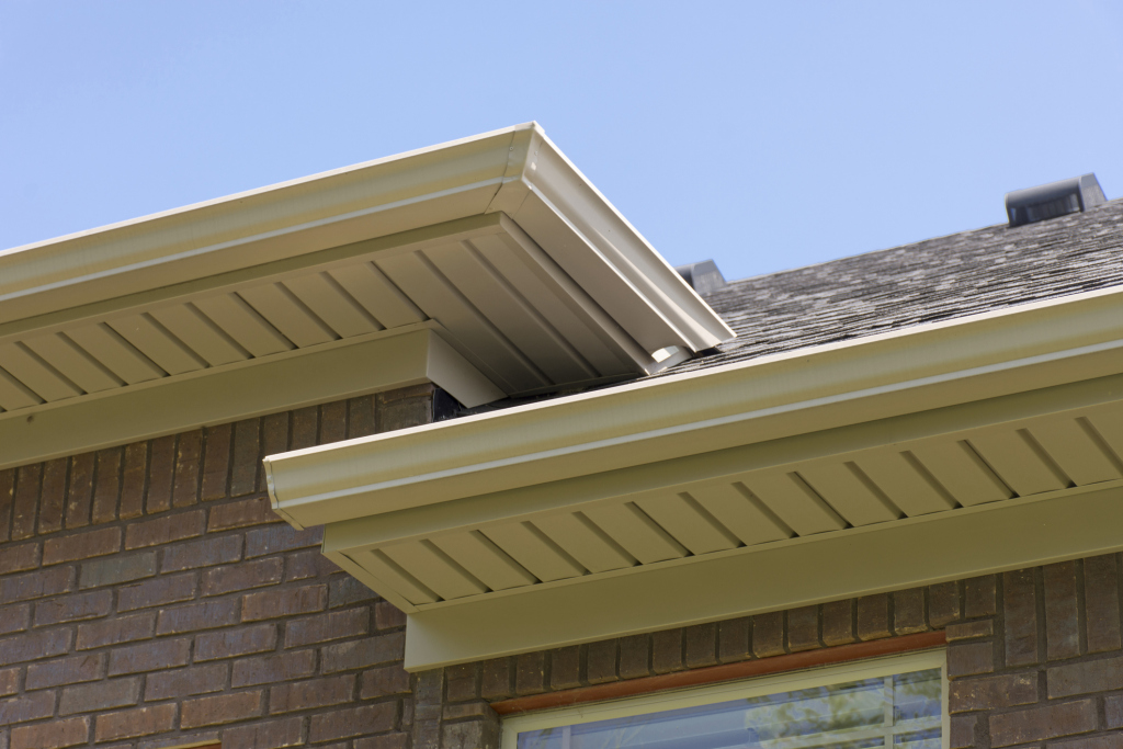 Close-up of house roof with gutters and soffit under blue sky.